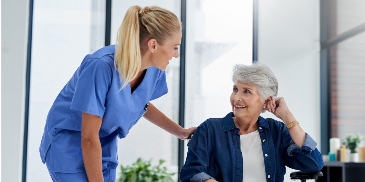 Krankenschwester mit Patientin, beide lächelnd.