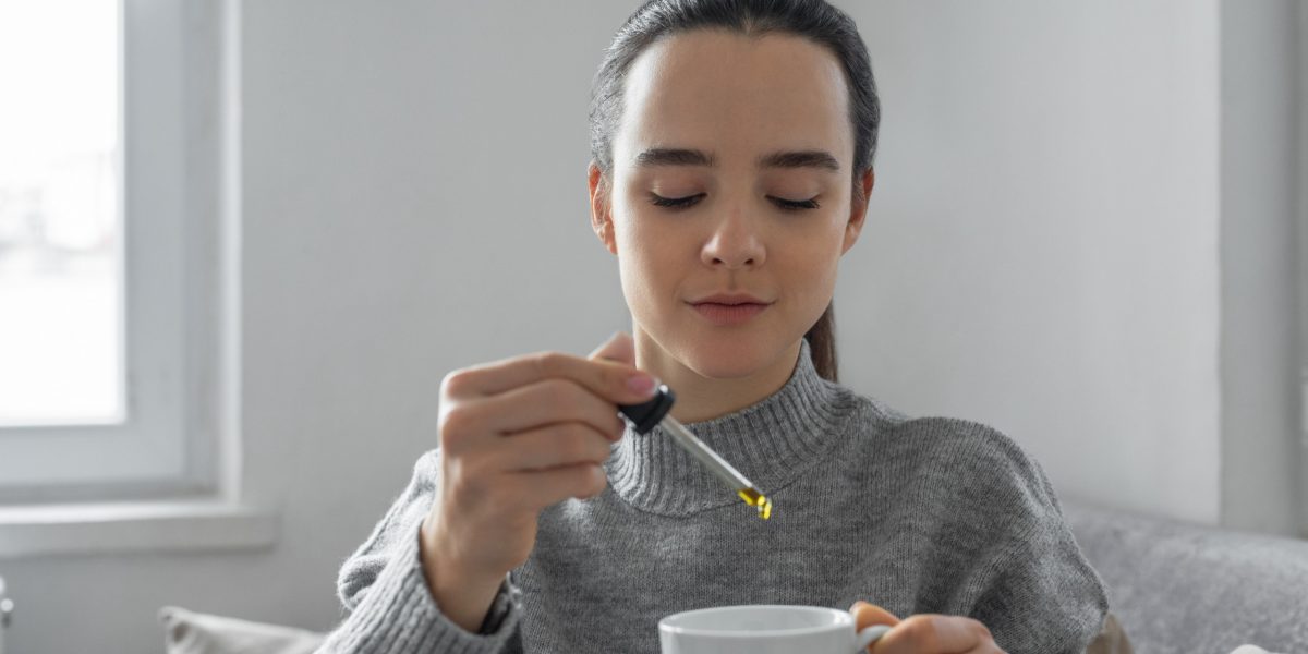 Junge Frau tropft CBD-Öl gegen Angst in ihre Tasse.
