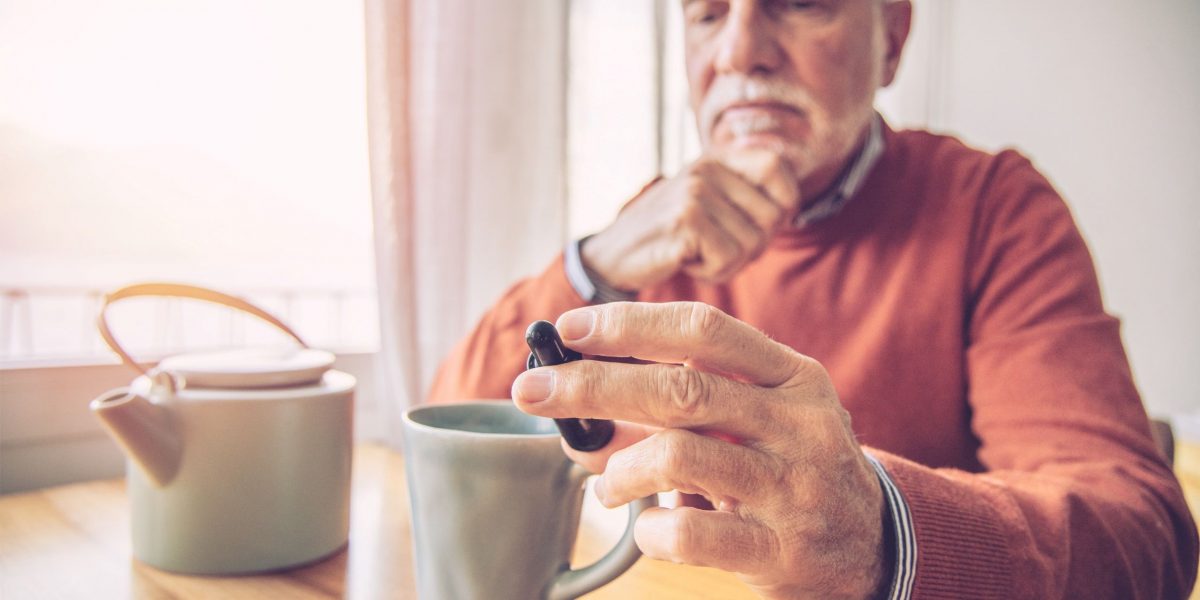 Senior mit Teetasse hält CBD-Öl in der Hand; negative Erfahrungen hst er noch keine gemacht