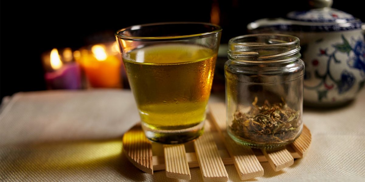 Ein Glas Tee und ein Glas mit getrockneten Kräutern zum Thema "CBD-Öl-Wirkung Psyche"