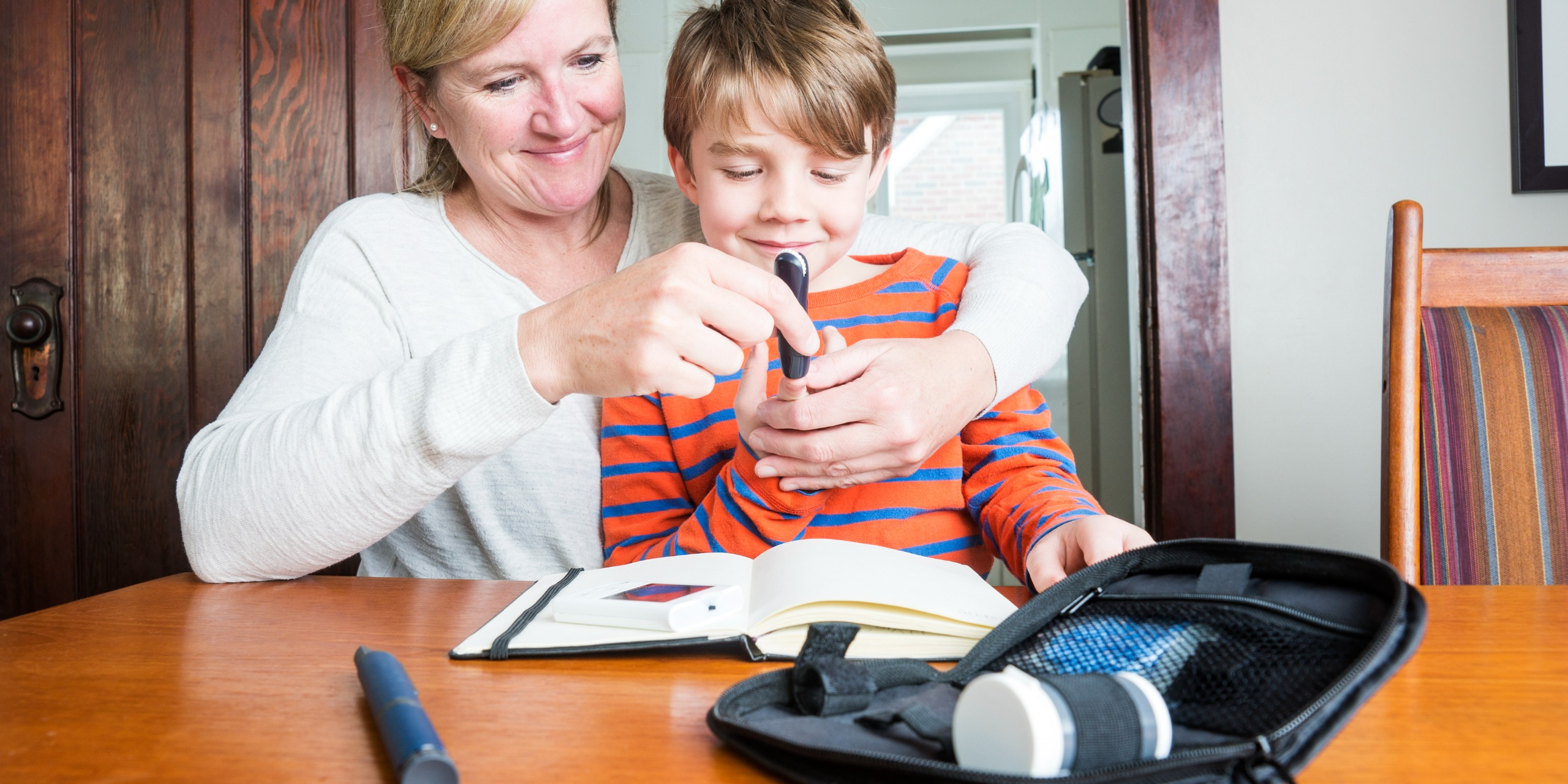 Kind mit Diabetes Typ 1 misst mit seiner Mutter den Blutzucker.