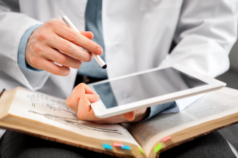Man in lab coat using digital tablet and open book